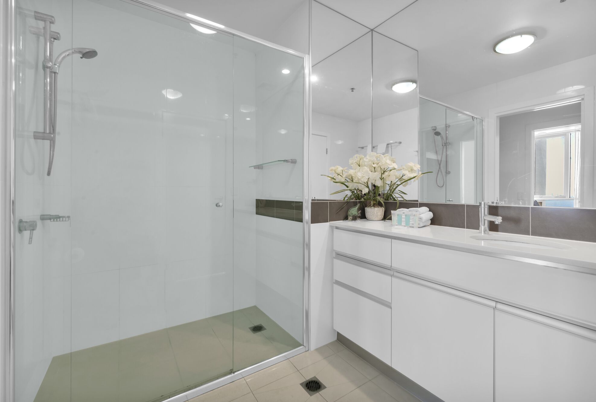 Un baño moderno con ducha envuelta en vidrio, un espejo grande y un tocador con lavabo y toallero.