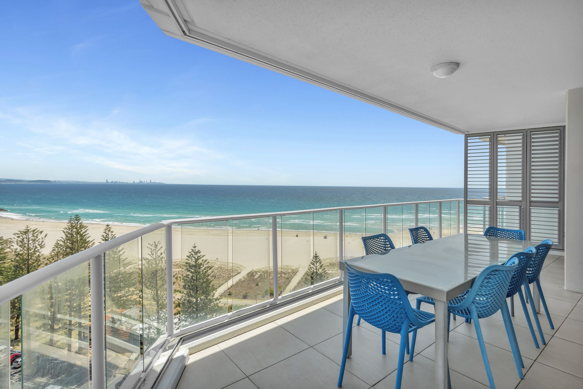 A balcony with a table and chairs, overlooking a beach and ocean.