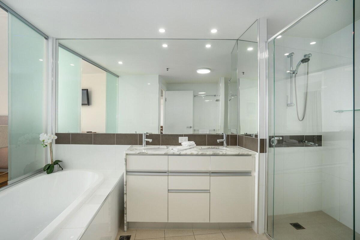 Un baño moderno con ducha de vidrio, un espejo grande y una bañera blanca.