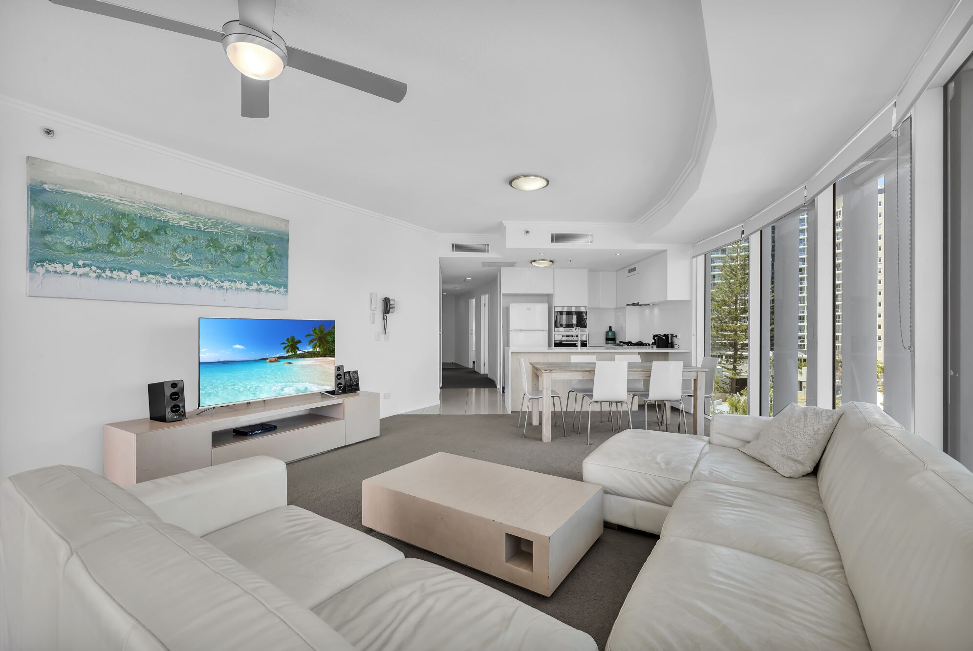 A modern living room with a flat-screen TV, white sofas, a coffee table, and a ceiling fan.