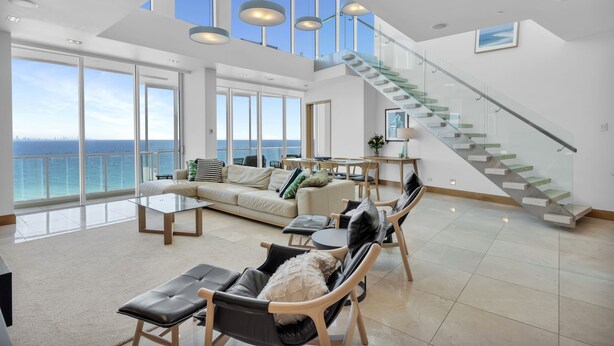 A spacious living area with a large window overlooking the sea, a modern staircase, and a cozy seating arrangement. - Reflection Tower Two (Coolangatta)