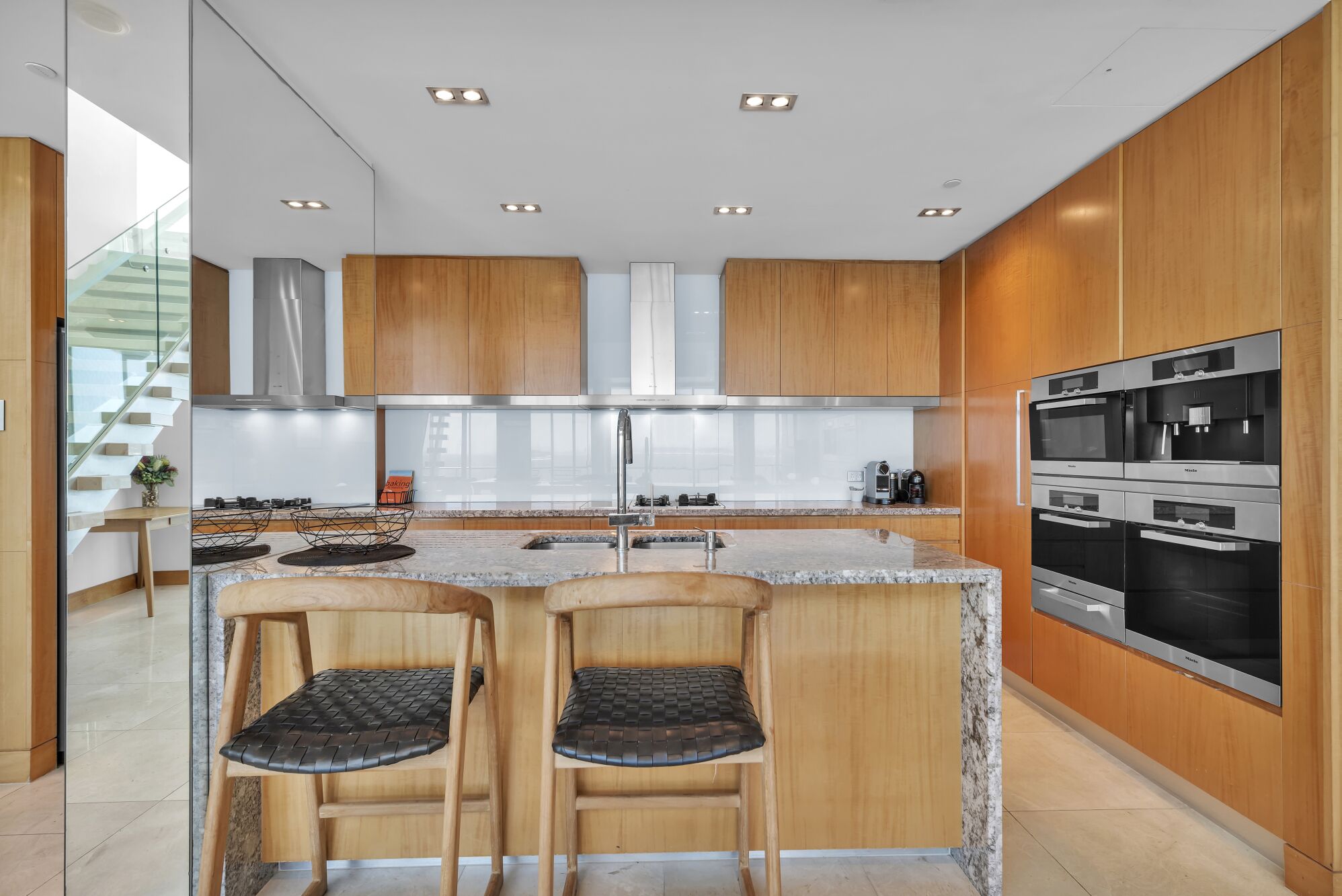 Une cuisine moderne avec des meubles en bois, des appareils en acier inoxydable et un îlot central doté de deux tabourets.