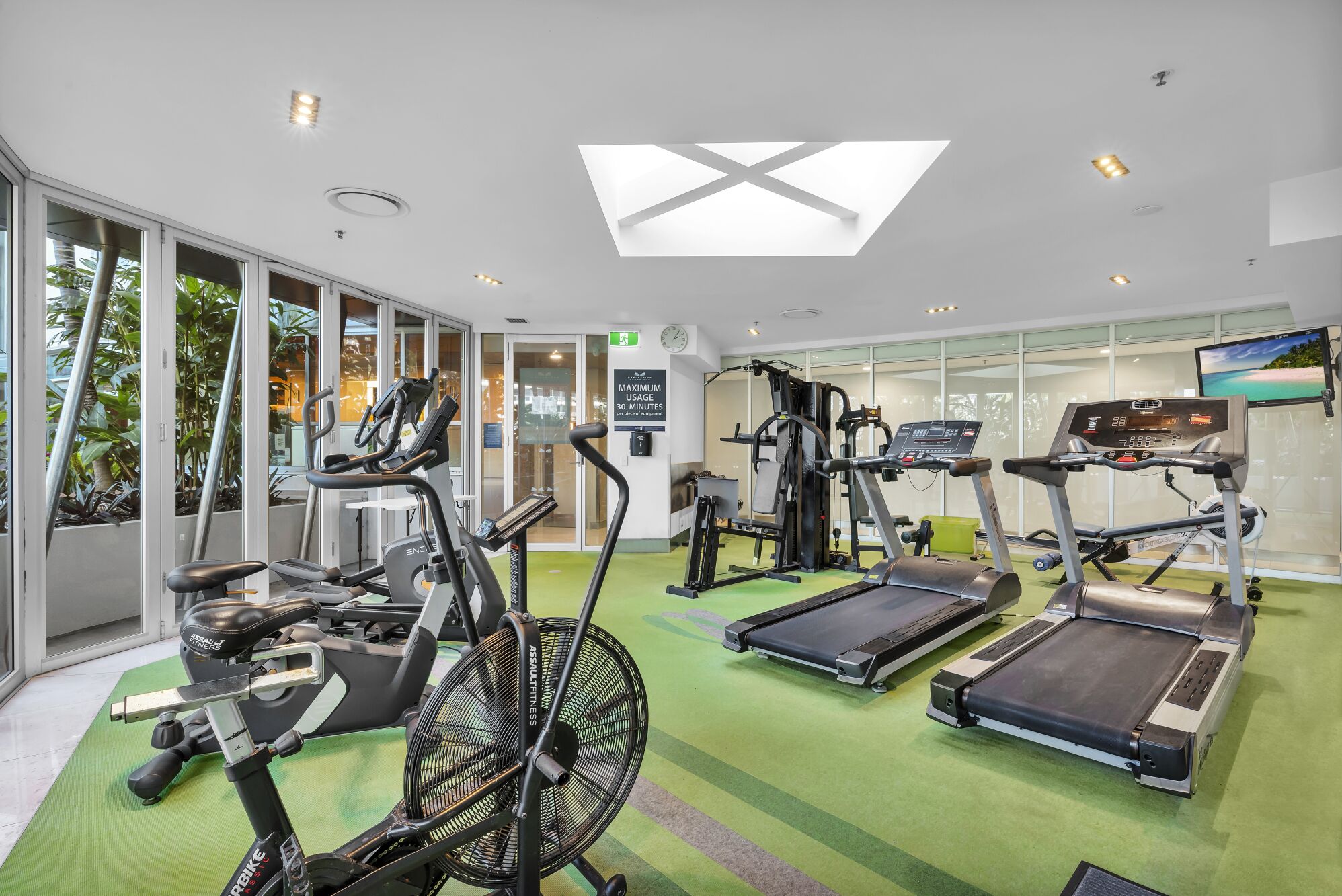 Une salle de sport équipée de tapis de course, de vélos elliptiques et d’un ventilateur.