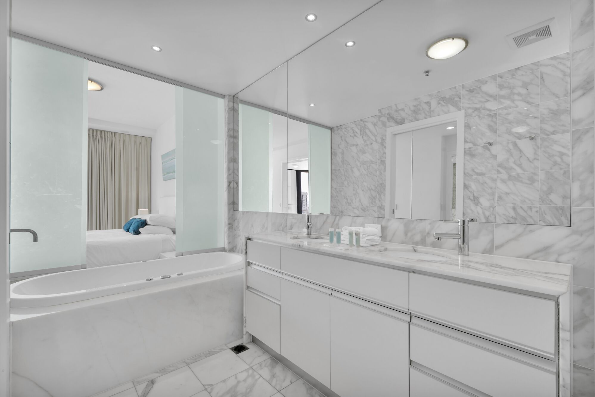 Une salle de bain moderne avec une grande baignoire, un meuble-lavabo avec un miroir et des murs en marbre.