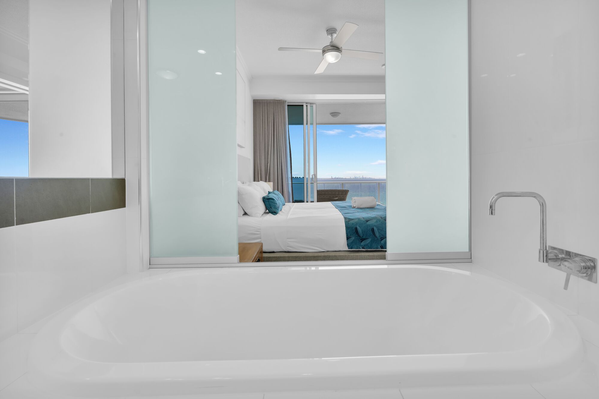 A modern hotel room with a large bathtub, a bed with a view, and a ceiling fan.