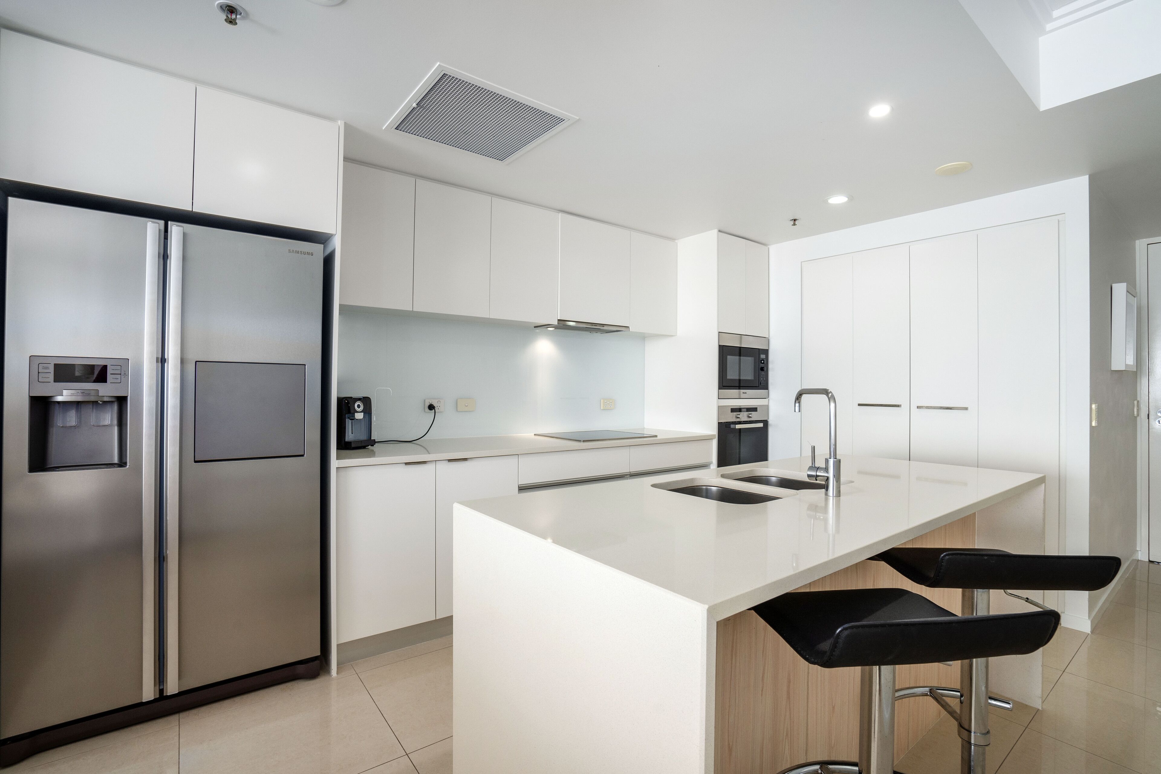 A modern kitchen with stainless steel appliances, a central island with bar stools, and white cabinetry.