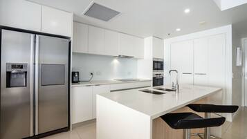 A modern kitchen with stainless steel appliances, a central island with bar stools, and white cabinetry.