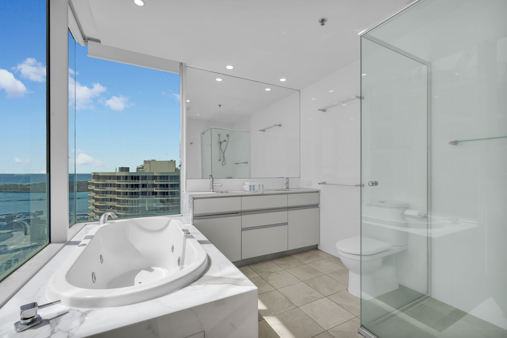 A modern bathroom with a glass shower enclosure, a large bathtub, and a view of the cityscape.