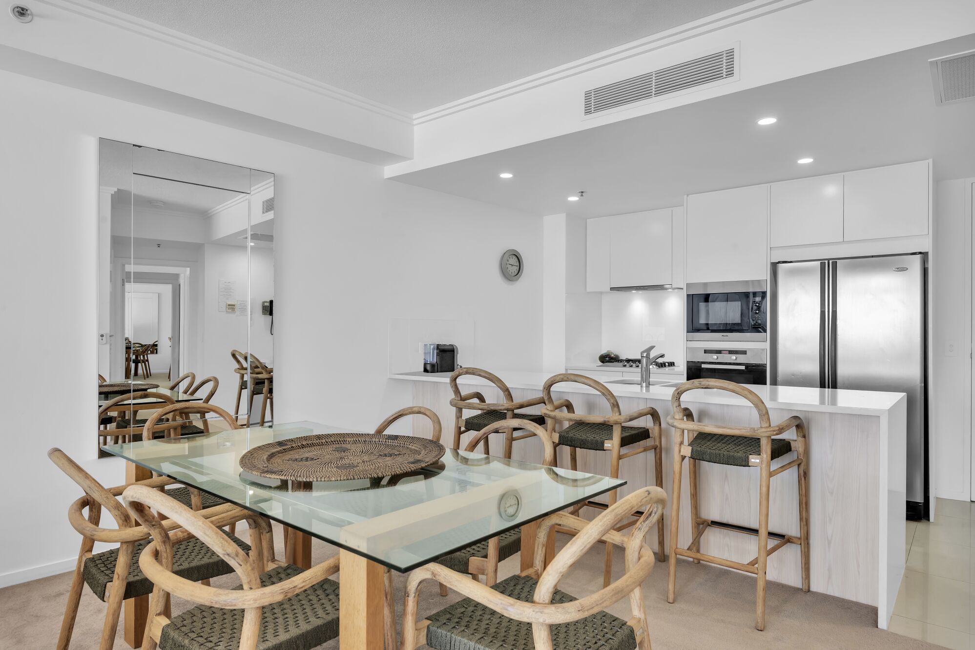 A modern kitchen with white cabinets, stainless steel appliances, and a glass dining table with woven placemats.