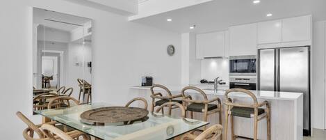A modern kitchen with white cabinets, stainless steel appliances, and a glass dining table with woven placemats.