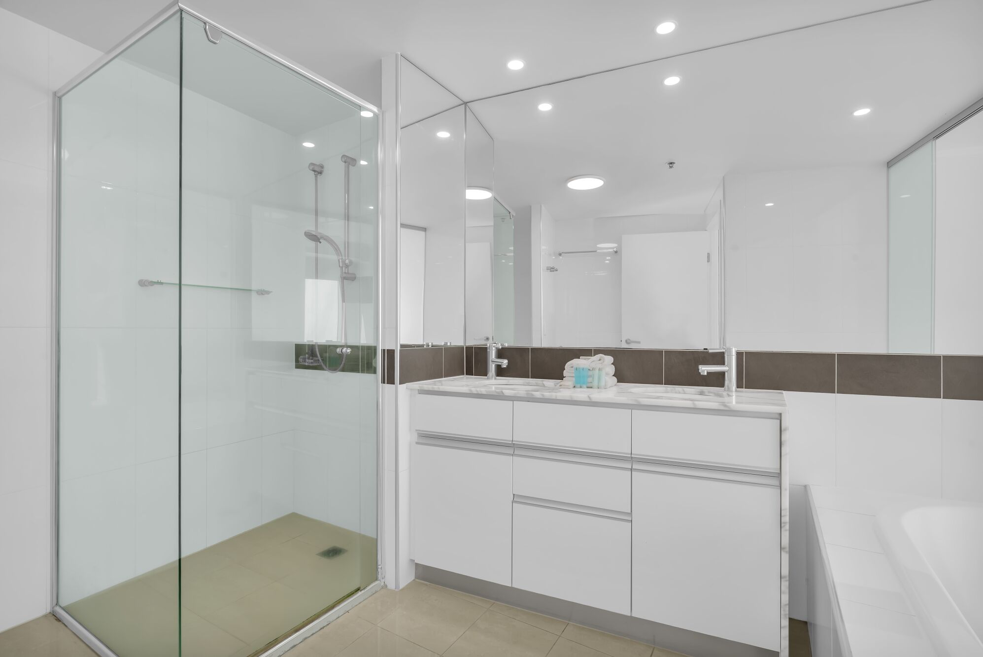 A modern bathroom with a glass shower enclosure, a white vanity with a marble countertop, and a large mirror above the sink.