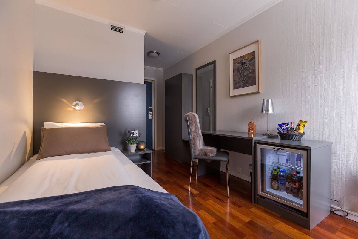 Une chambre d’hôtel moderne équipée d’un lit, d’un bureau, d’une chaise, d’un mini-réfrigérateur et d’un miroir.