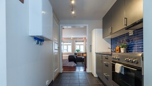 Une cuisine moderne avec un carrelage foncé, des appareils électroménagers en acier inoxydable et une vue sur une chambre à coucher avec un lit et une fenêtre.
