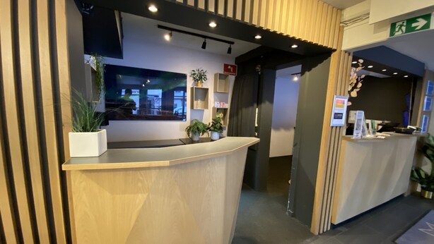 Un espace d’accueil avec un comptoir en bois, des plantes en pot et une vue sur l’extérieur.