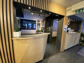 Un área de recepción con un mostrador de madera, plantas en macetas y vistas al exterior.