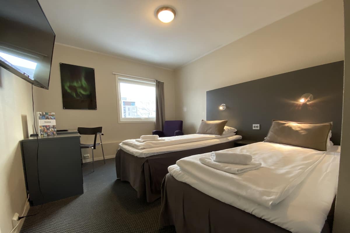 Une chambre d’hôtel avec deux lits, un bureau, une chaise, une télévision et une fenêtre avec des rideaux.
