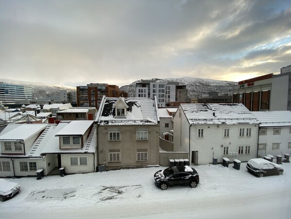 A snowy urban area with buildings and parked cars.