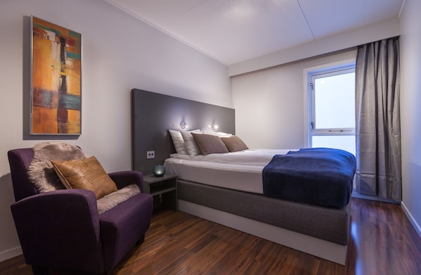 Relax in a stylish room with a large bed, armchair, and side table, featuring a beautiful view through large windows.