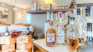 A bar area with various bottles of alcohol, wooden crates labeled 'MACULAN', and a clock tower in the background. - Hotel Belvedere (Thiene)