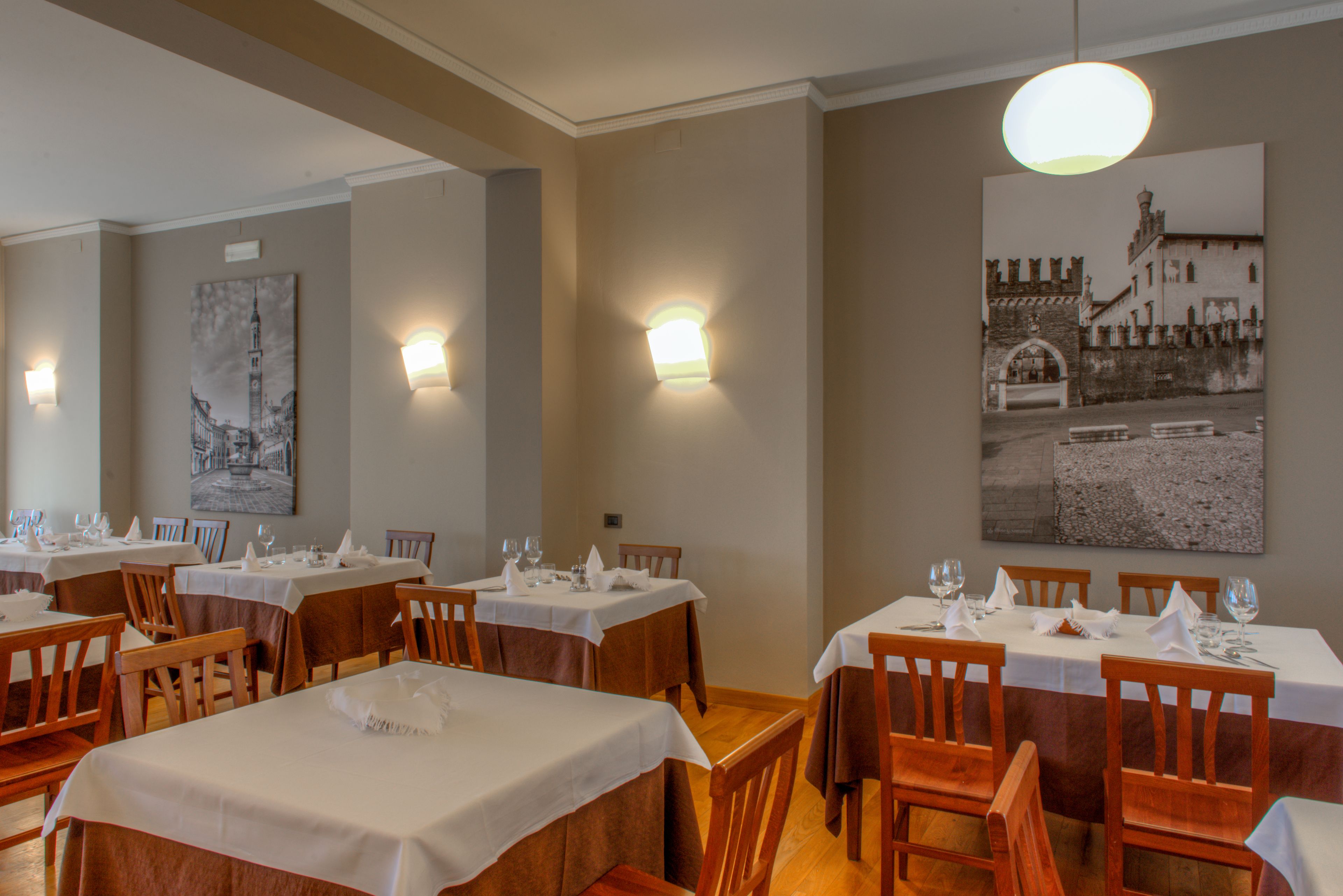 A restaurant with multiple tables set for dining, each with white tablecloths and wooden chairs.