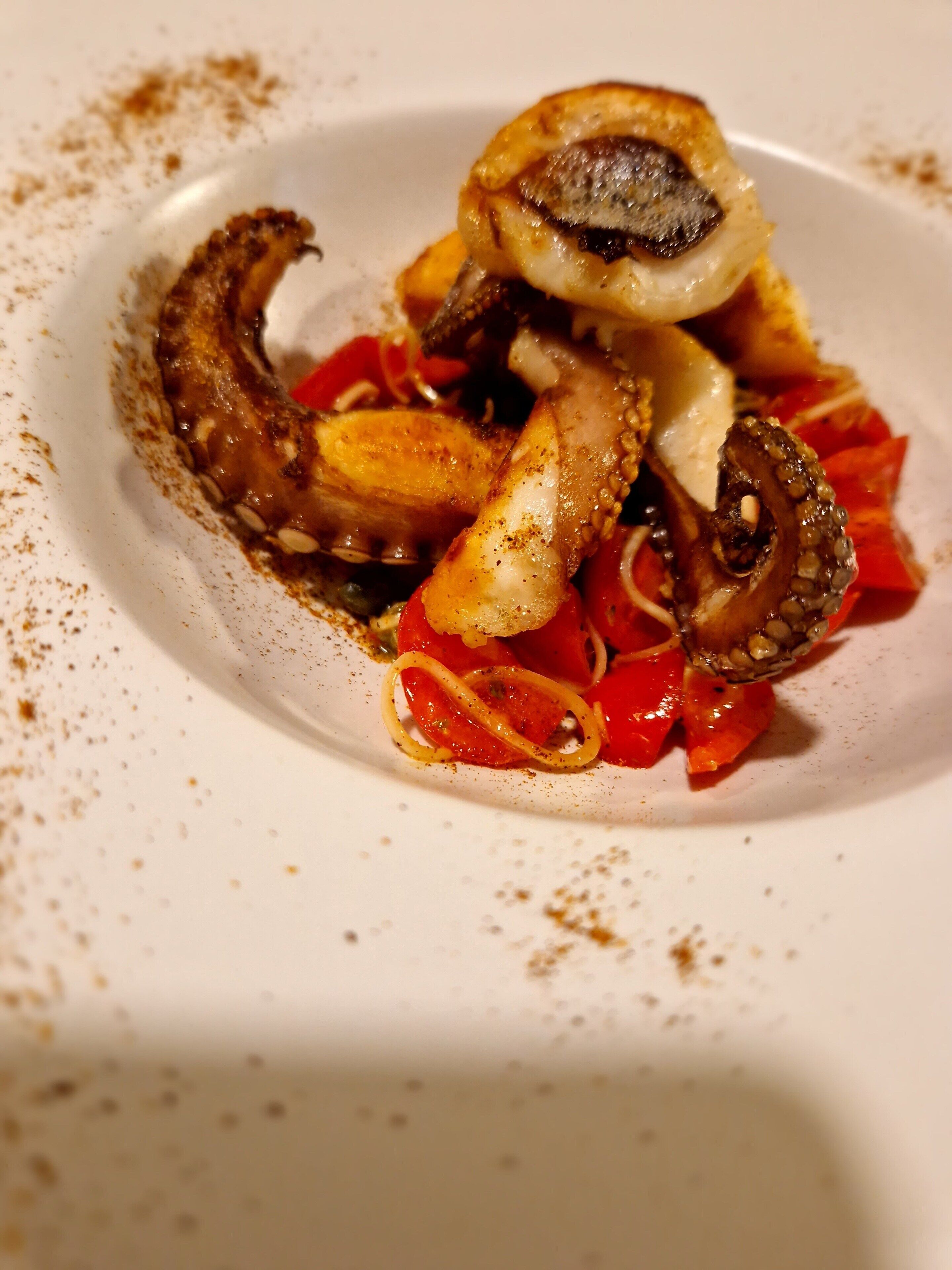 En vit tallrik med grillad bläckfisk, skivade tomater och lite kryddor.