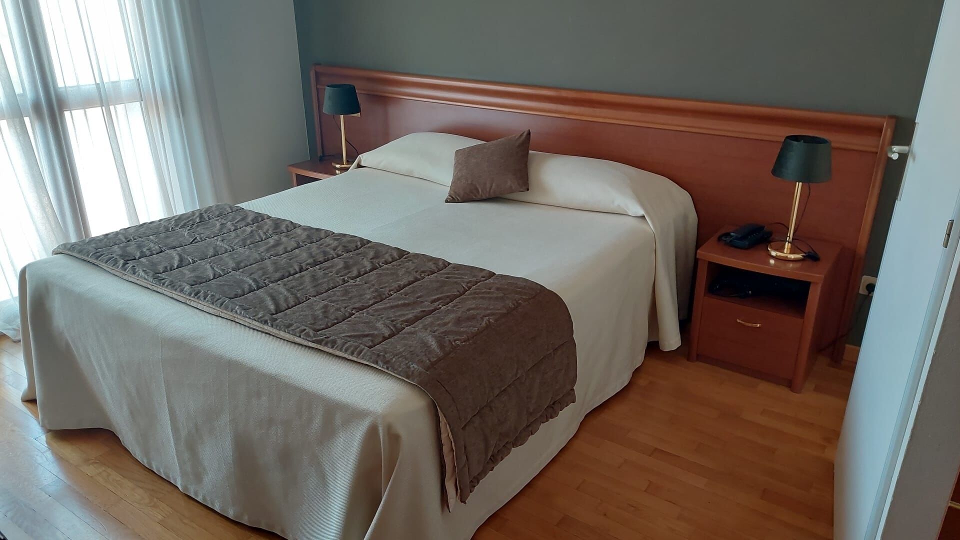 A neatly made bed with a brown blanket, two bedside lamps, and a wooden nightstand with a drawer.
