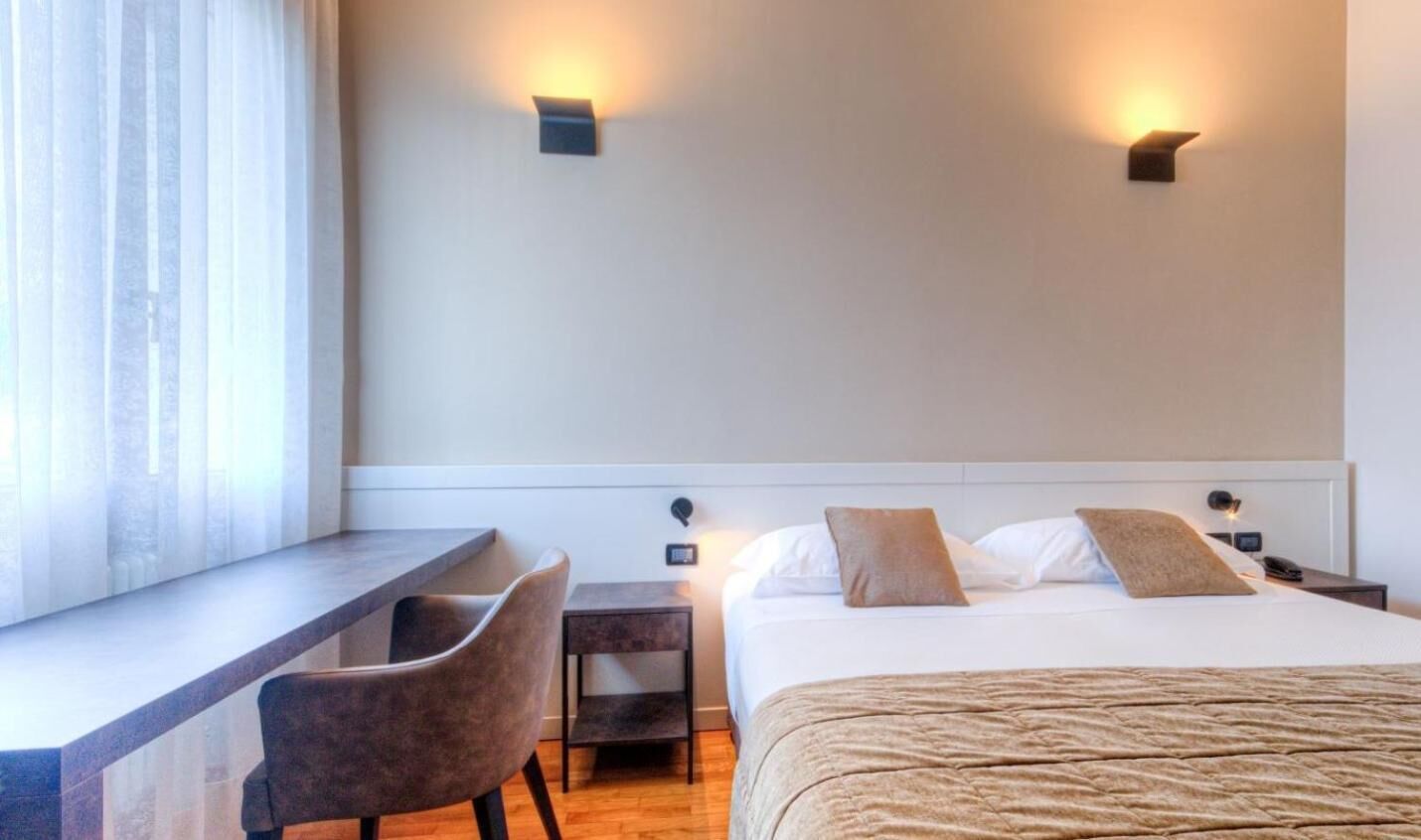 A hotel room with a bed, a desk, and two wall-mounted lights.