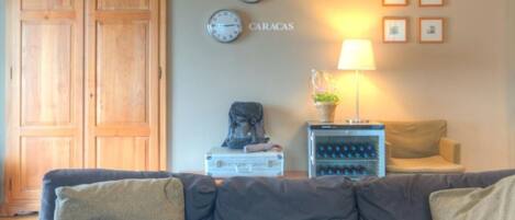 A living room with a grey sofa, a wooden wardrobe, a lamp, and wall clocks labeled with city names.