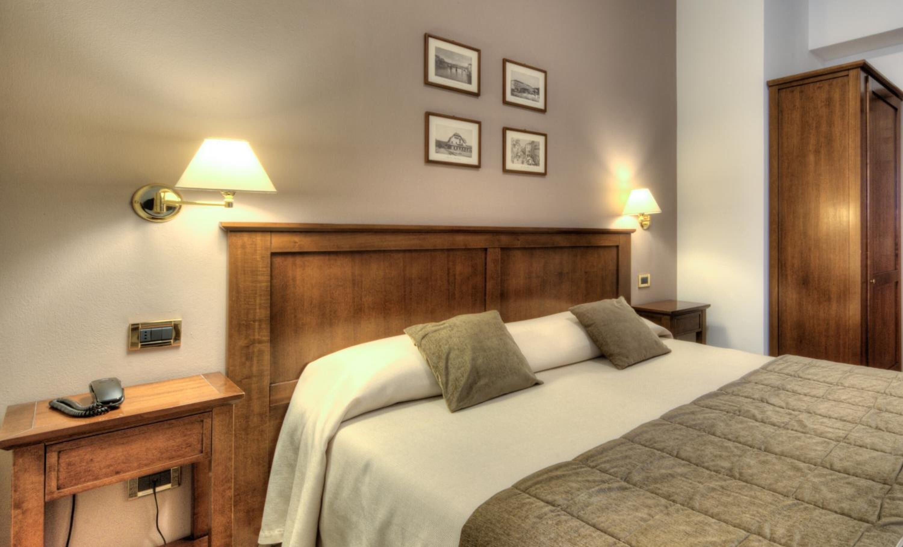 A neatly arranged hotel room with a wooden headboard, a bed with two pillows, a bedside table with a lamp, and a telephone.