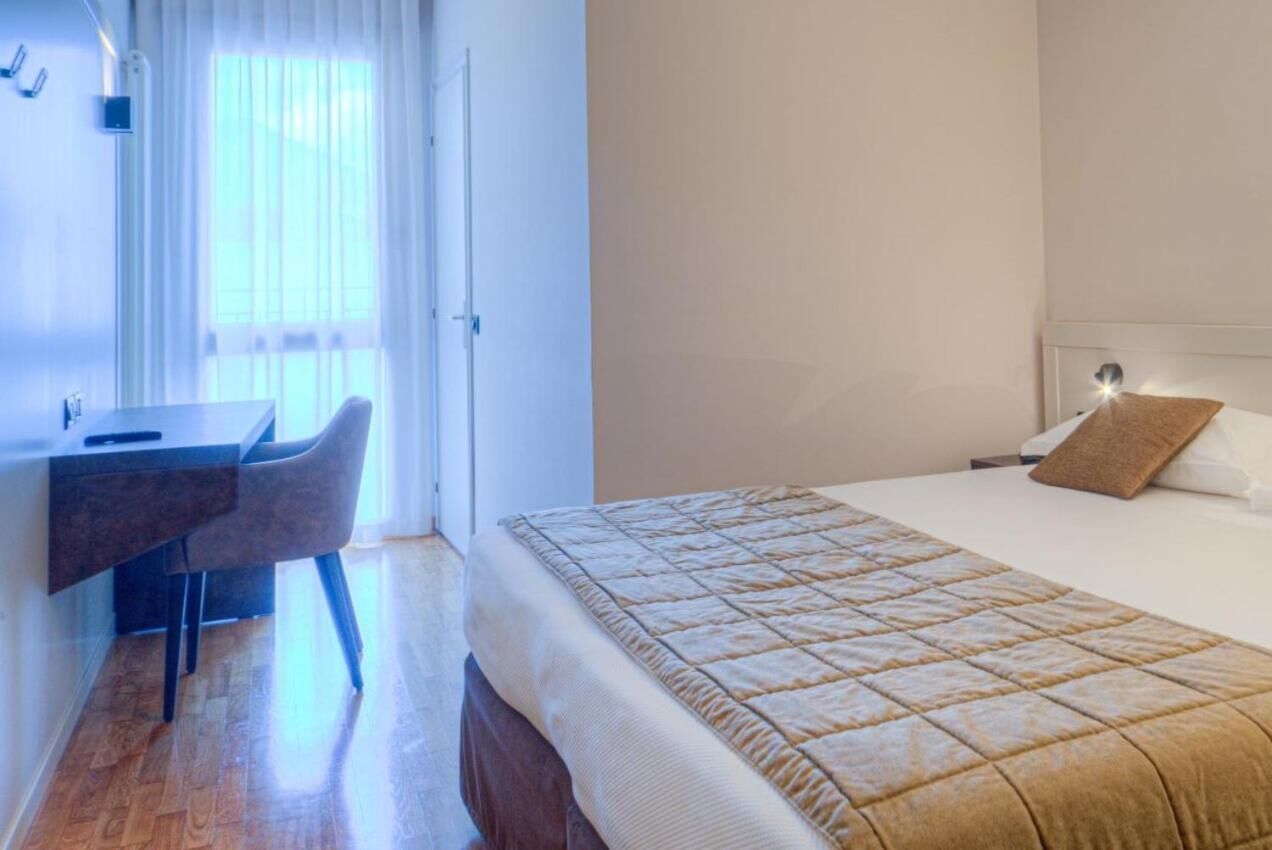 A hotel room with a bed, a desk, and a chair.