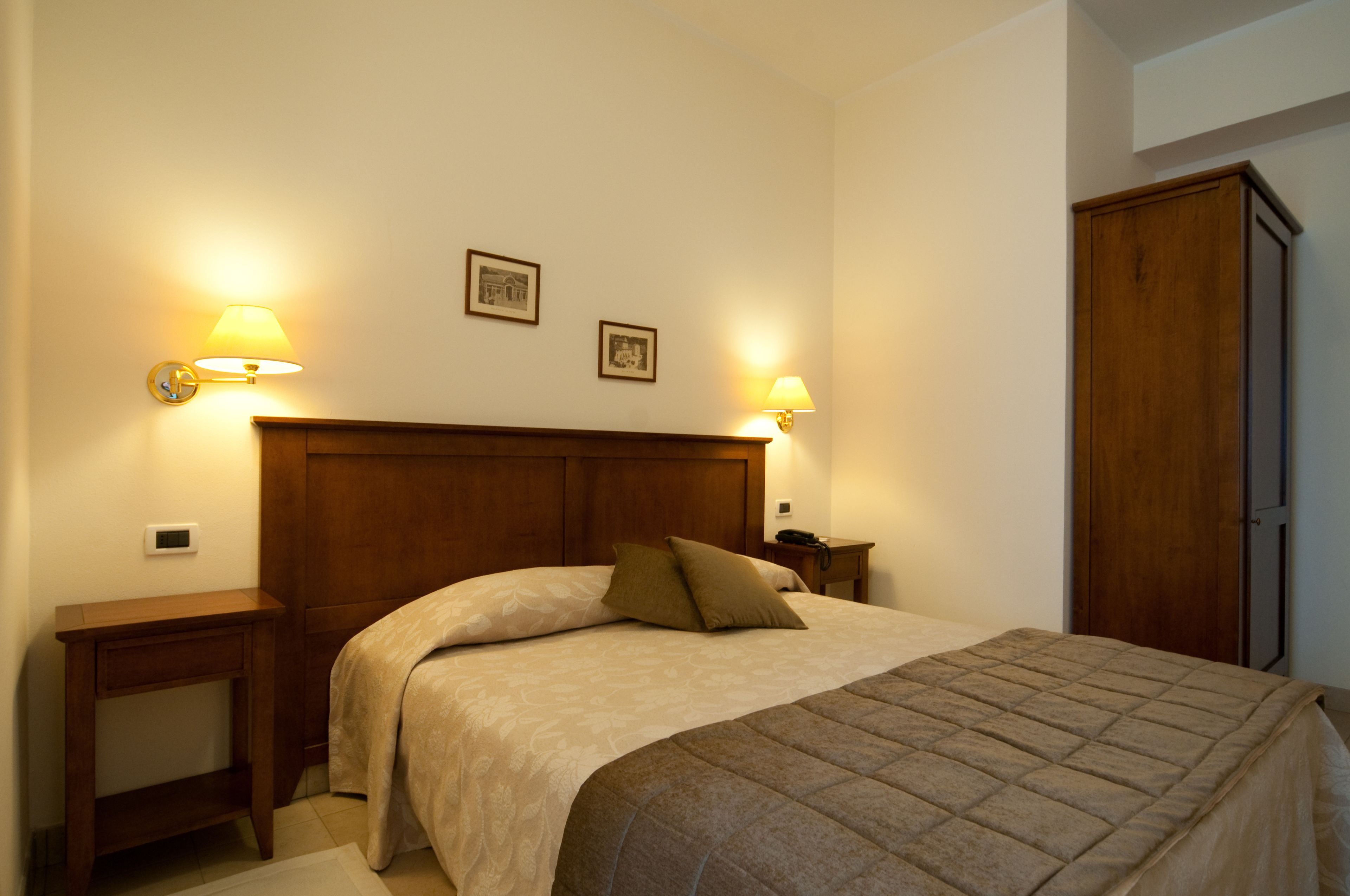 Una cama bien tendida con cabecera de madera, dos lámparas de noche y una mesita de noche con un teléfono.