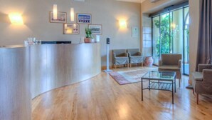 A reception area with a wooden reception desk, a sofa, a coffee table, and a floor lamp. - Hotel Belvedere (Thiene)