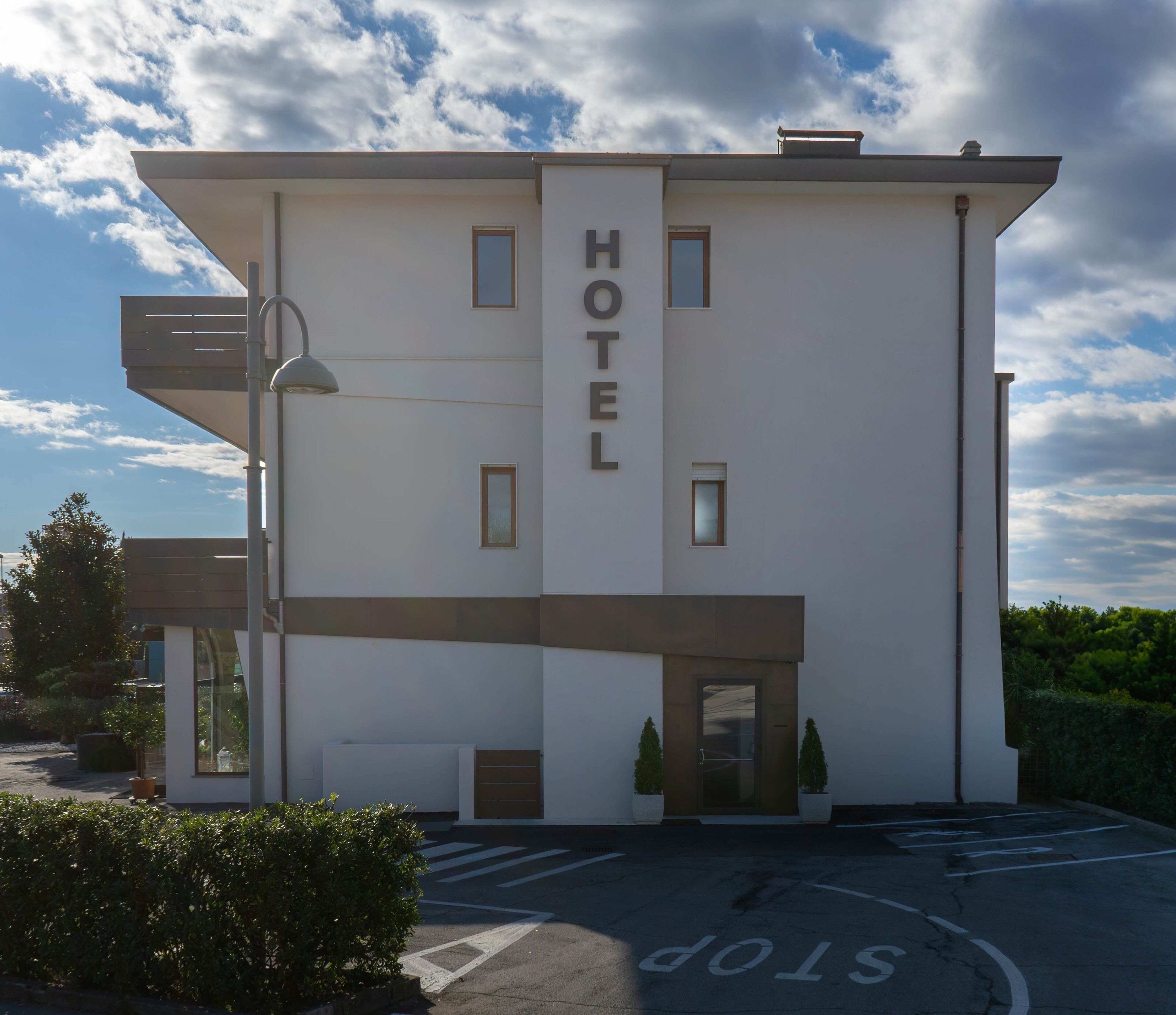 A modern hotel with a flat facade, a prominent 'HOTEL' sign, and a parking area with a 'STOP' marking.