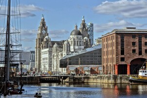 A historic waterfront with a tall clock tower, a domed building, and a red brick building with arches.