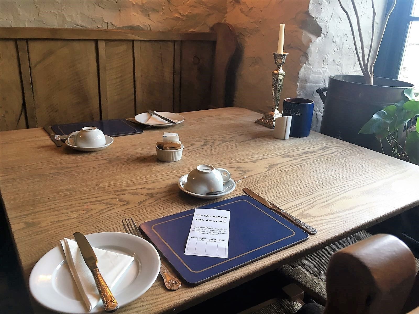 A wooden dining table set with plates, cutlery, a menu, and a candle.
