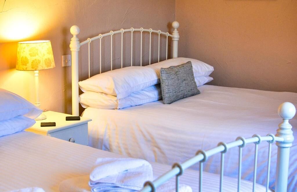 Un lit bien fait, avec une literie blanche et un oreiller gris, une lampe de chevet et une tête de lit en métal blanche.
