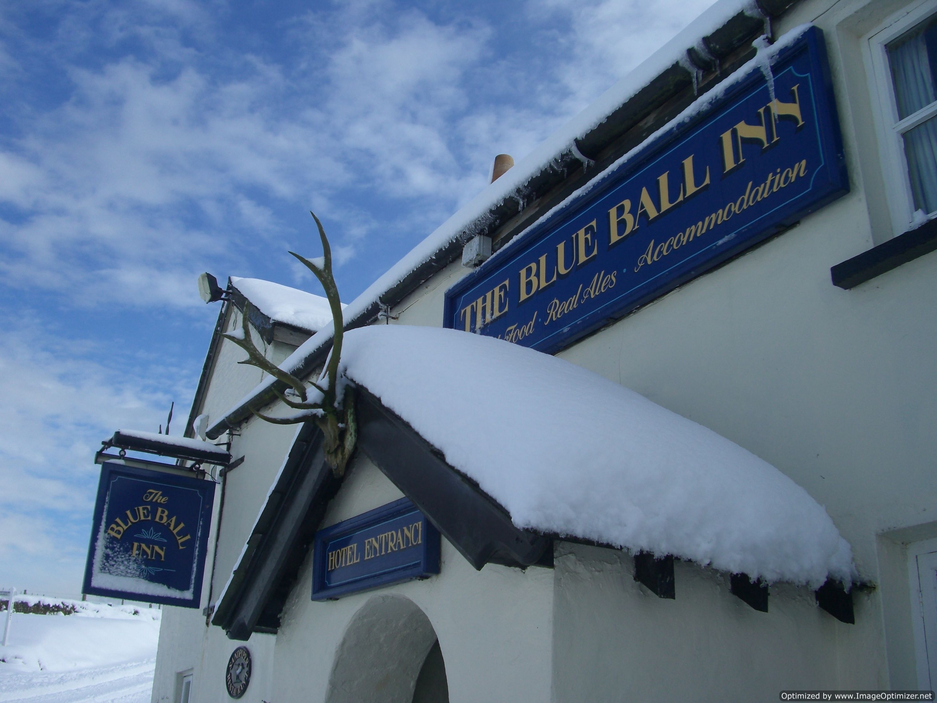A hotel entrance with a sign reading "The Blue Ball Inn" and another sign above it stating "The Blue Ball Inn" with additional text "Food, Real Ales, Accommodation".