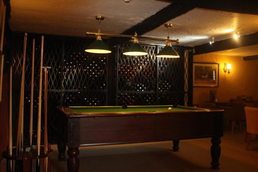 A billiards room with a pool table, green lamps, and a wine rack in the background.