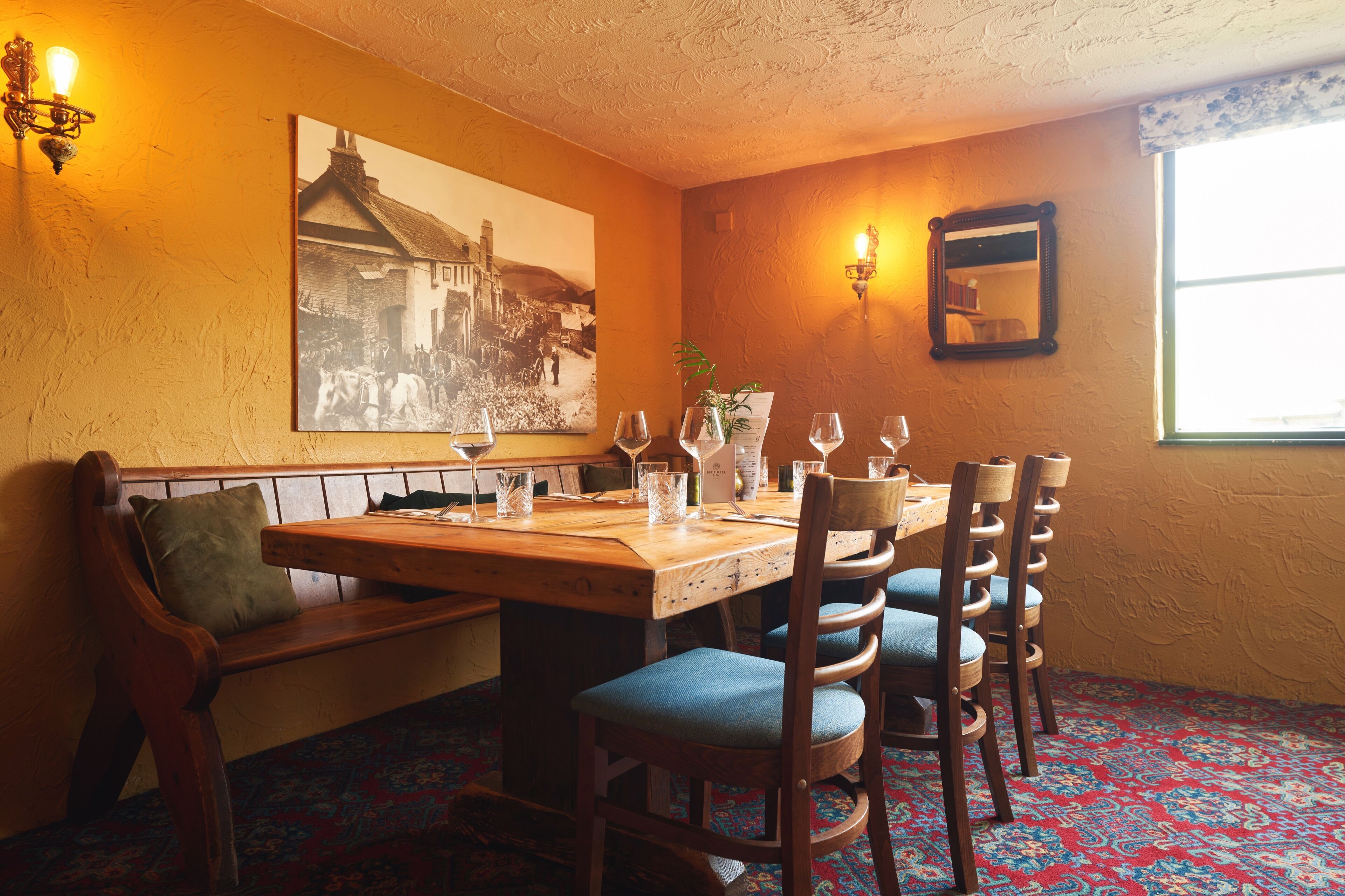 A dining area with a wooden table set for four, a bench, and a wall-mounted picture.
