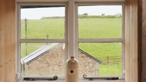 Ein Fenster mit Blick auf ein grünes Feld und ein Steinhaus.