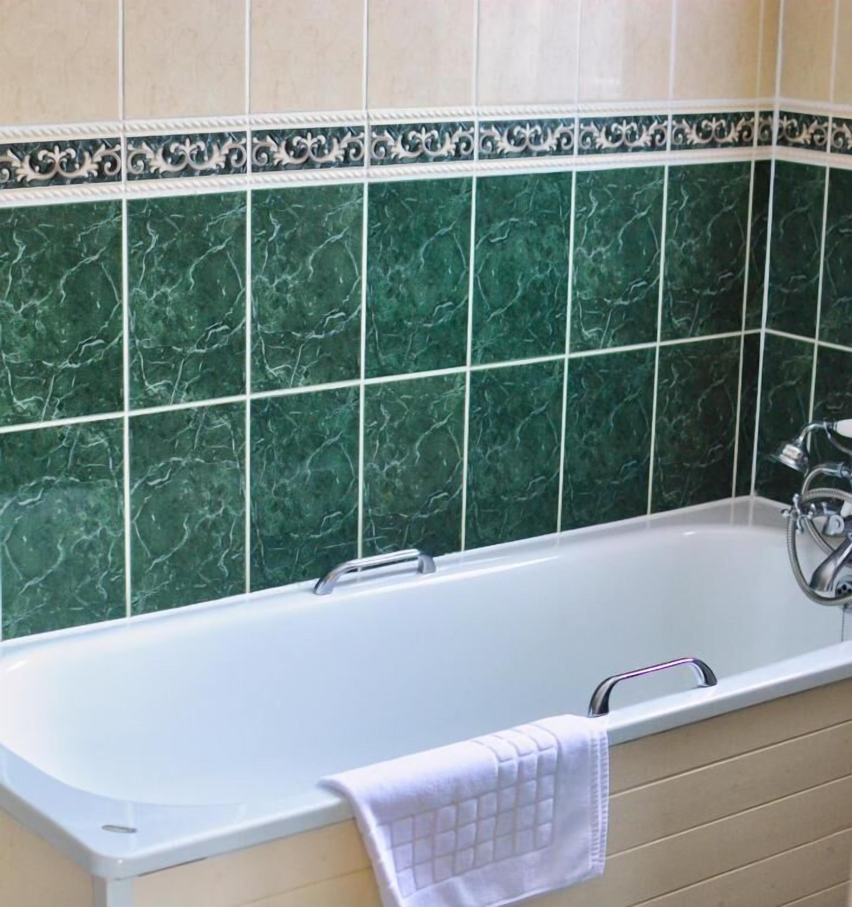 A bathroom with a white bathtub, green marble tiles, and a beige vanity.