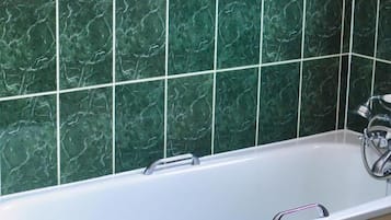 A bathroom with a white bathtub, green marble tiles, and a beige vanity.