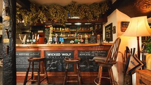Eine Barbereich mit Holzhockern, einer Kreidetafel mit der Speisekarte und einem Schild für 'Wicked Wolf Distillery'.