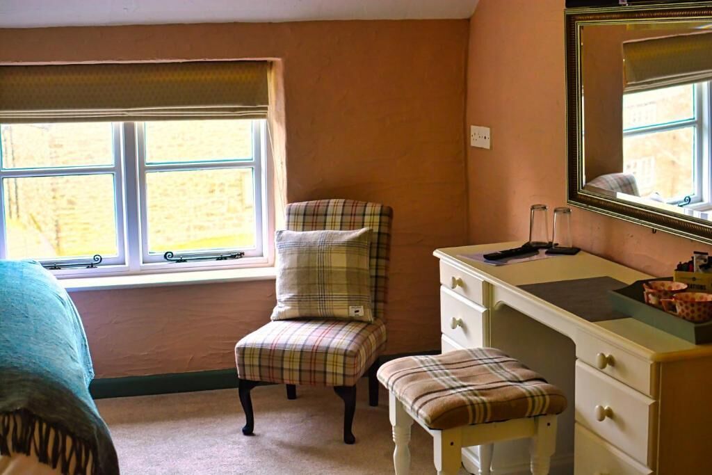 A bedroom with a plaid chair, a small bench, a dresser, and a mirror.