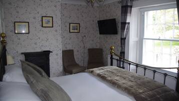 Ein Schlafzimmer mit einem Bett, zwei Sesseln, einem Kamin, einem Fernseher und einem Fenster mit Vorhängen.