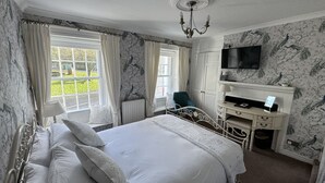 A bedroom with a large bed, a desk, a chair, a television, and a window with curtains. - Brunswick House (Barnard Castle)