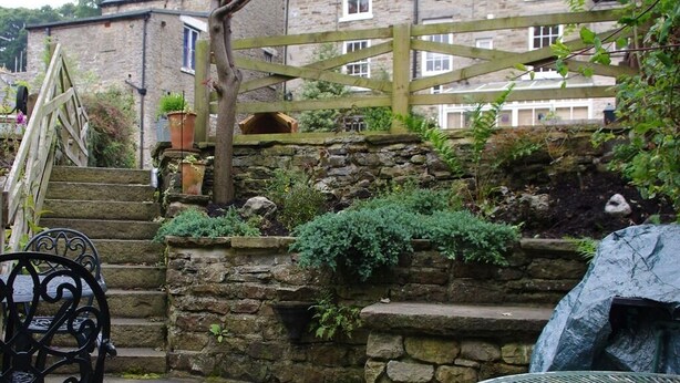 A stone staircase leading to a stone wall with plants, a wooden gate, and a metal table with a chair. - Brunswick House (Barnard Castle)