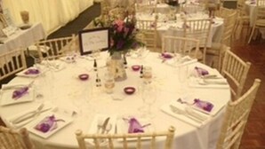 A round dining table with white tablecloth, surrounded by wicker chairs. - Coach House Hotel (Royston)