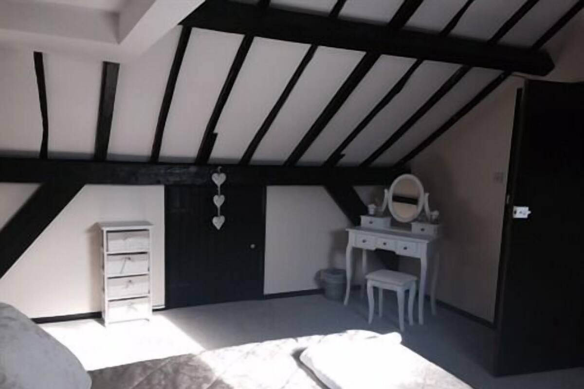 A bedroom with a sloped ceiling, a bed, a dresser, a vanity with a mirror, and a door.