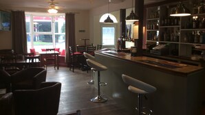 A bar area with stools, a counter, and shelves of bottles. - Coach House Hotel (Royston)